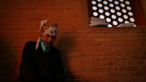 Man with headscarf standing against brick wall