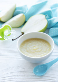 Bowl with baby food and pears on table