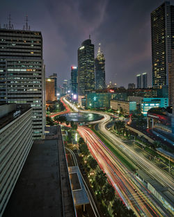 Light trails on road amidst buildings against sky at night