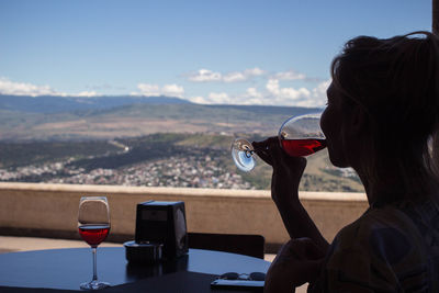 Woman drinking wine at table against landscape
