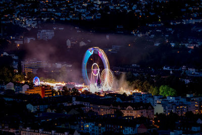 Illuminated ferris wheel in city against sky at night