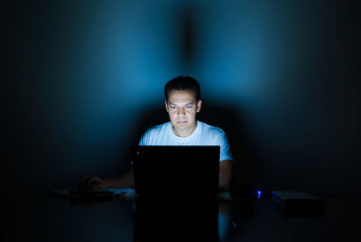 Portrait of young man using laptop in dark room