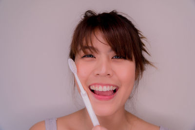 Portrait of young woman with toothbrush against gray background