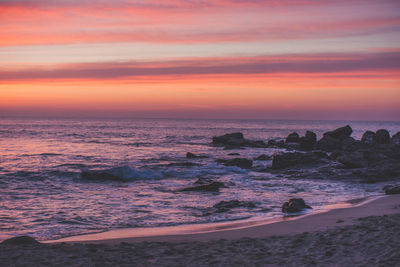 Scenic view of beach against cloudy sky during sunset