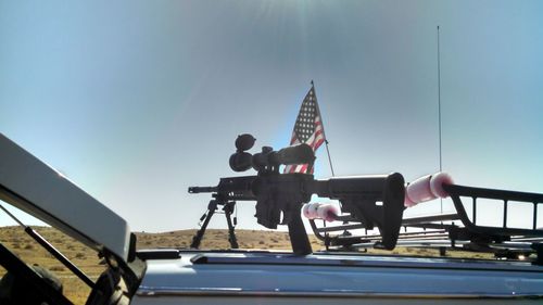 Machine guns on vehicle by american flag against sky