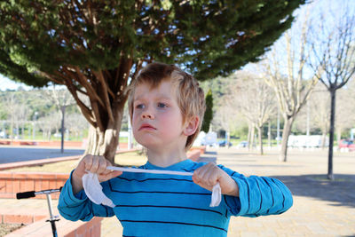 A disgruntled blond boy pulls a white rope with his hands. a five-year-old boy is in a bad mood.
