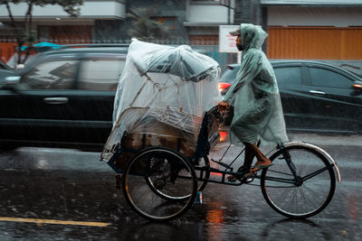 Man riding tricycle on wet street during rainy season