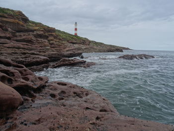 Rocky sea shore against cloudy sky