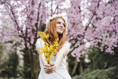 Beautiful woman standing by cherry blossom against tree