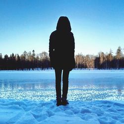 Rear view of woman standing on frozen lake against clear sky