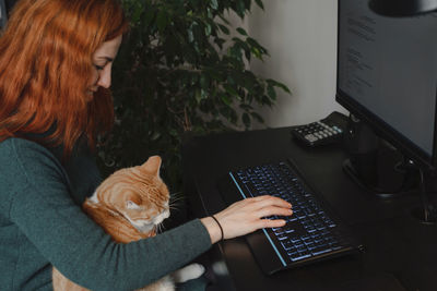 Woman working on keyboard and computer with cat on her laps. freelancer doing her work at home with