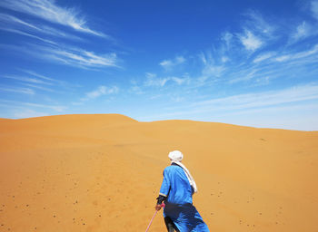 Man on sand dune in desert against sky