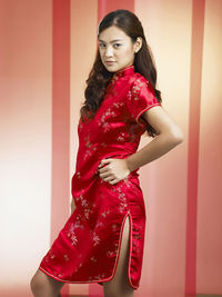 Portrait of confident woman with hand on hip standing against backdrop