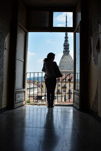 Rear view of silhouette man standing by window in building