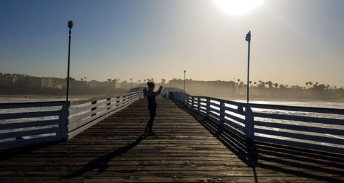 Man walking on pier by street against sky