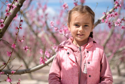 Portrait of cute girl standing against cherry trees