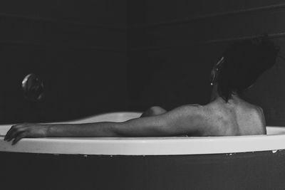 Rear view of shirtless woman sitting in bathtub at home