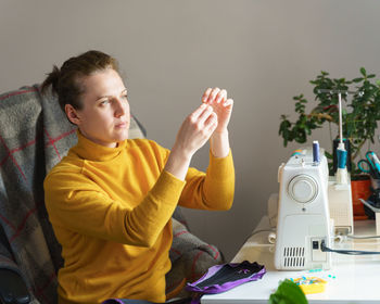 Busy female seamstress inserting thread into needle while working remotely at her workspace at home