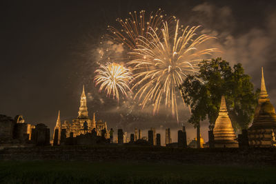 Firework display over illuminated building against sky at night