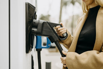 Young woman holding charging cord at electric car station