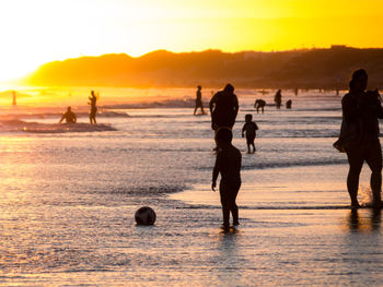 Silhouette people on beach against sky during sunset