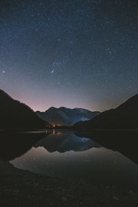 Scenic view of lake and mountains against sky at night