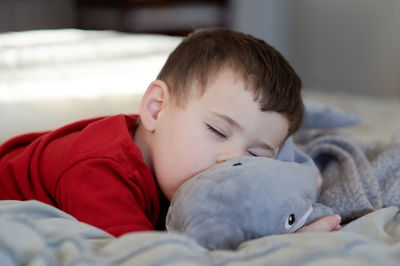 Young boy taking a nap on the bed using his plush toy as a pillow