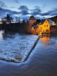 River flowing amidst buildings against sky at dusk