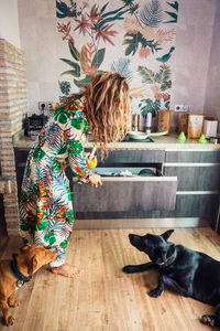Loyal dog resting on floor near barefoot woman in colorful dress cooking healthy lunch in light kitchen at home