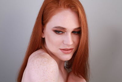 Close-up of beautiful woman with redhead against gray background