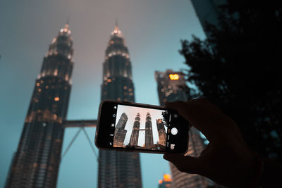 Low angle view of hand holding tower against buildings in city