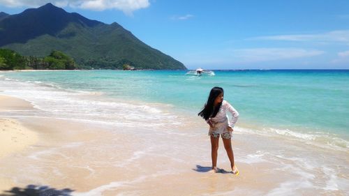 Full length of girl looking away while standing at beach against sky