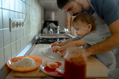 Father and son rolling pizza dough together in kitchen at home