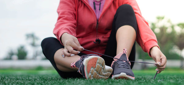 Low section of young woman tying shoelace while sitting on grass