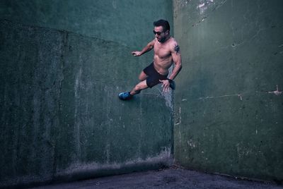 Full length of shirtless man jumping in concrete wall