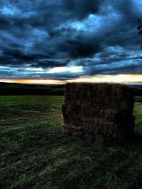 Hay bales on field against dramatic sky