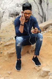 Full length of young man holding camera while sitting outdoors