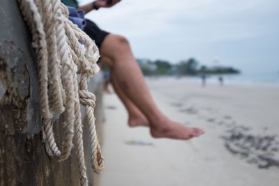 Low section of person sitting on wall at beach