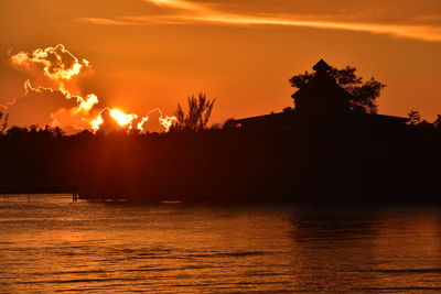 Silhouette trees by sea against orange sky