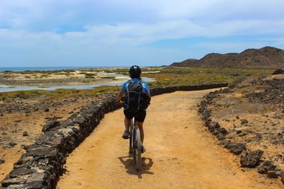Rear view of man walking on road against sky