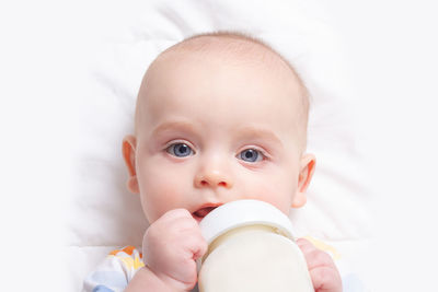 Portrait of cute baby holding milk bottle lying on bed at home