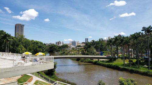 Bridge over river amidst trees in park against sky