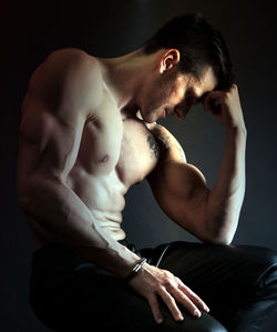 Side view of muscular man with tattoo sitting against gray background