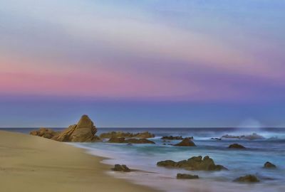 Rocks on beach against sky during sunset