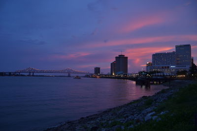 Bridge over river by illuminated buildings against sky at sunset - new orleans, missisipi river, lou