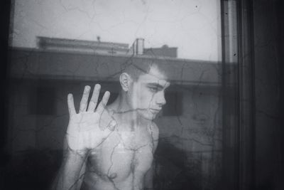 Close-up of shirtless teenage boy with hand on glass window