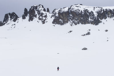 Hiker walking on snow covered field by mountains