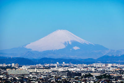 Cityscape and snowcapped mountains against clear blue sky