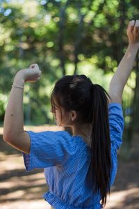 Rear view of woman with arms raised in park