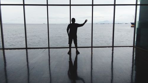 Silhouette man looking at sea through window